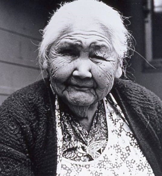 An old woman looks into the camera in this black and white photograph.